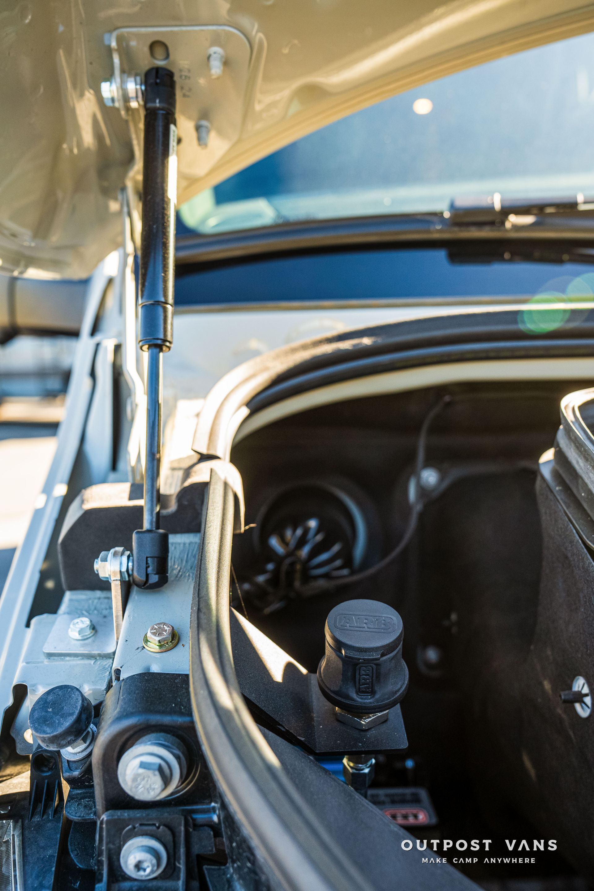 Open car hood with a black strut, and engine components visible.