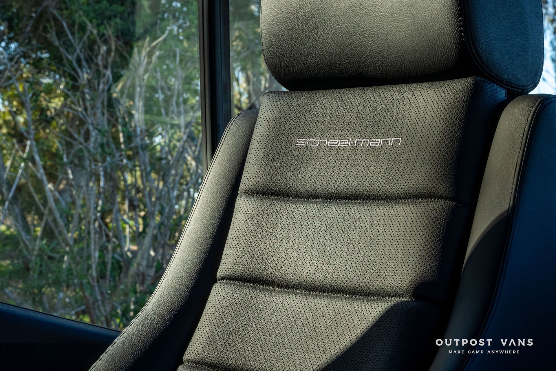 Black car seat with stitched horizontal lines; window with blurred trees. 