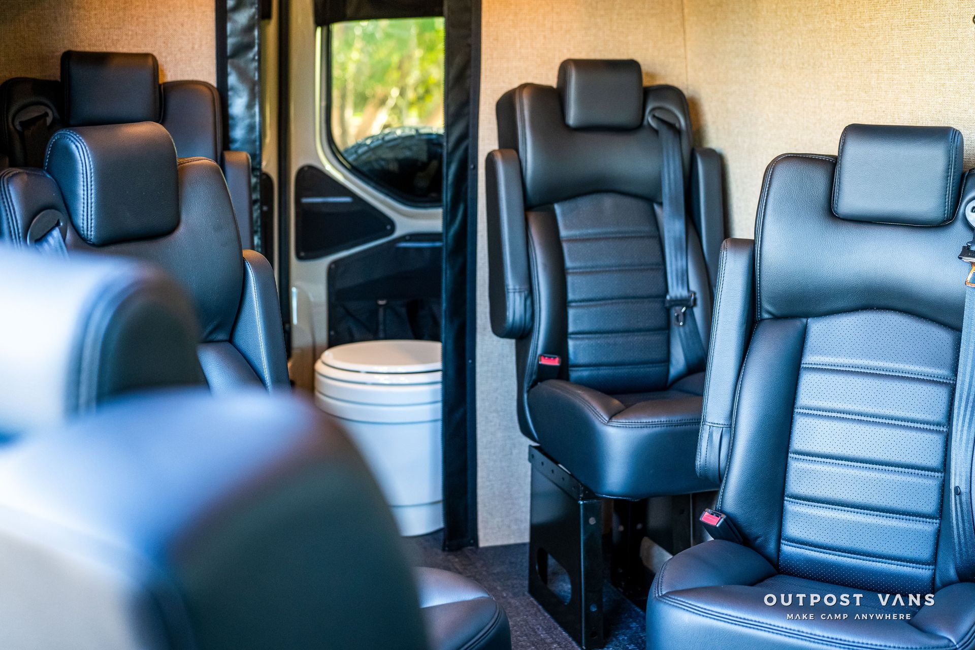 Interior of a converted van with black leather seating and a toilet.