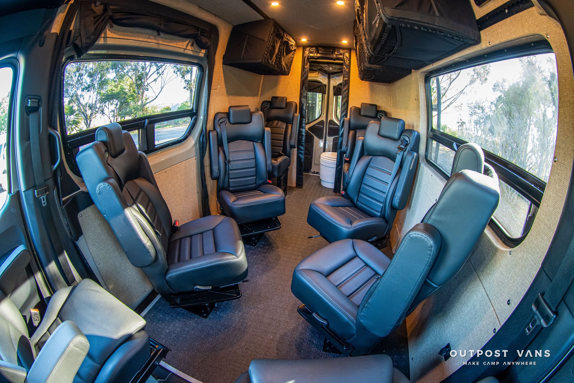 Interior view of a converted van with black leather seats, luggage storage, and windows.