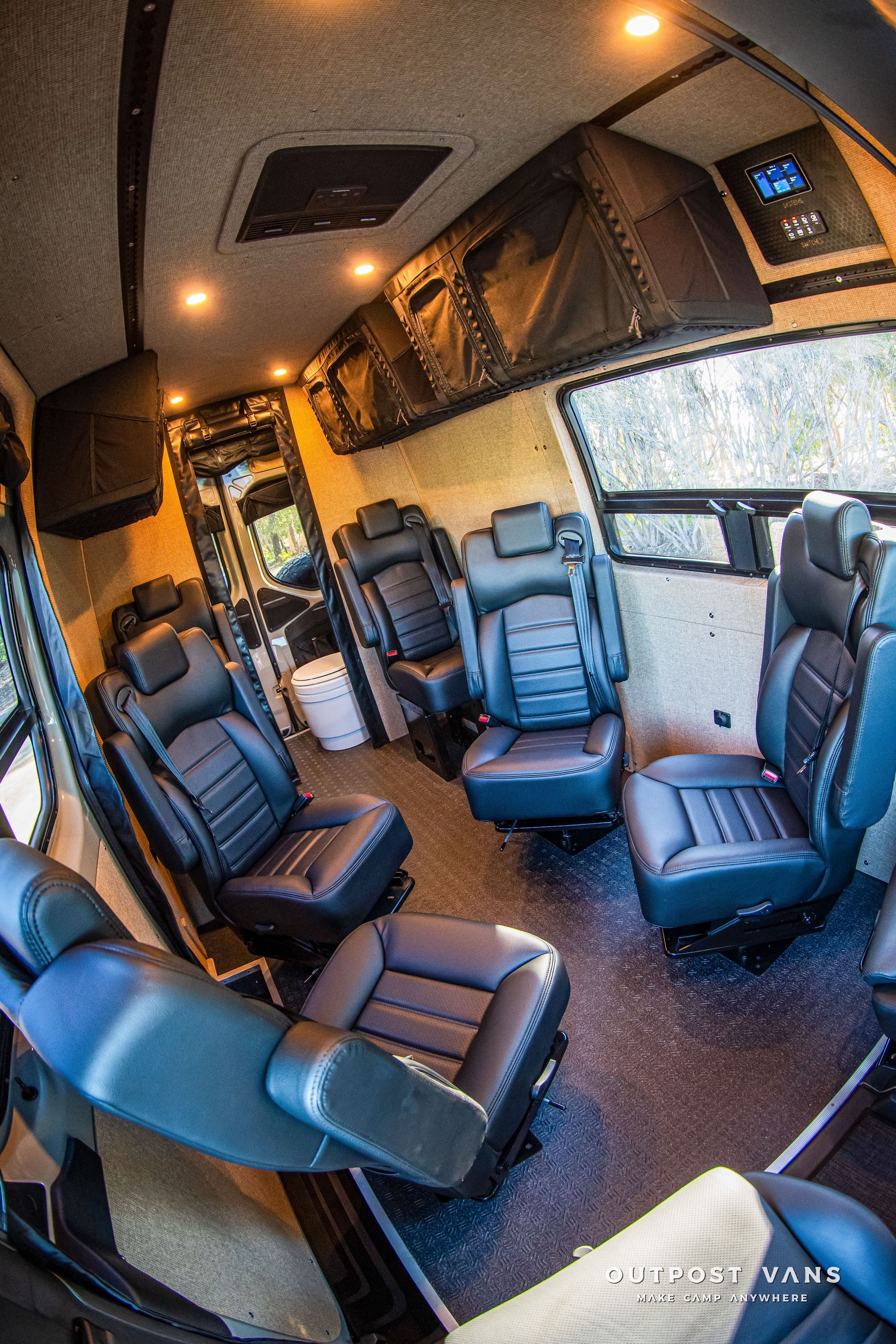 Interior of a luxury van with black leather seats, dark flooring, and overhead lighting.