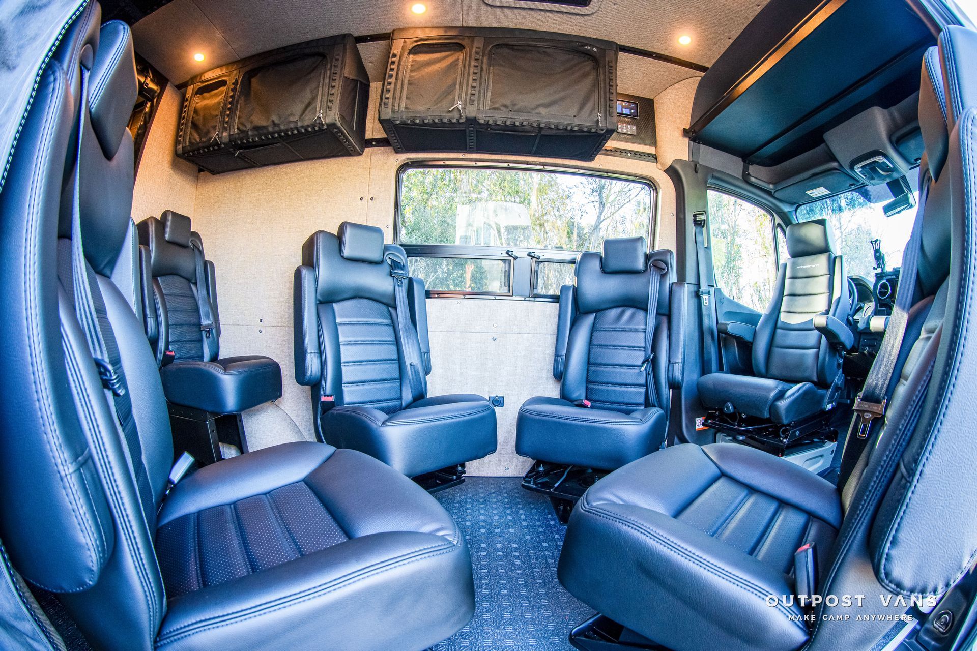 Interior of a van with black leather seats, overhead storage, and a large window.