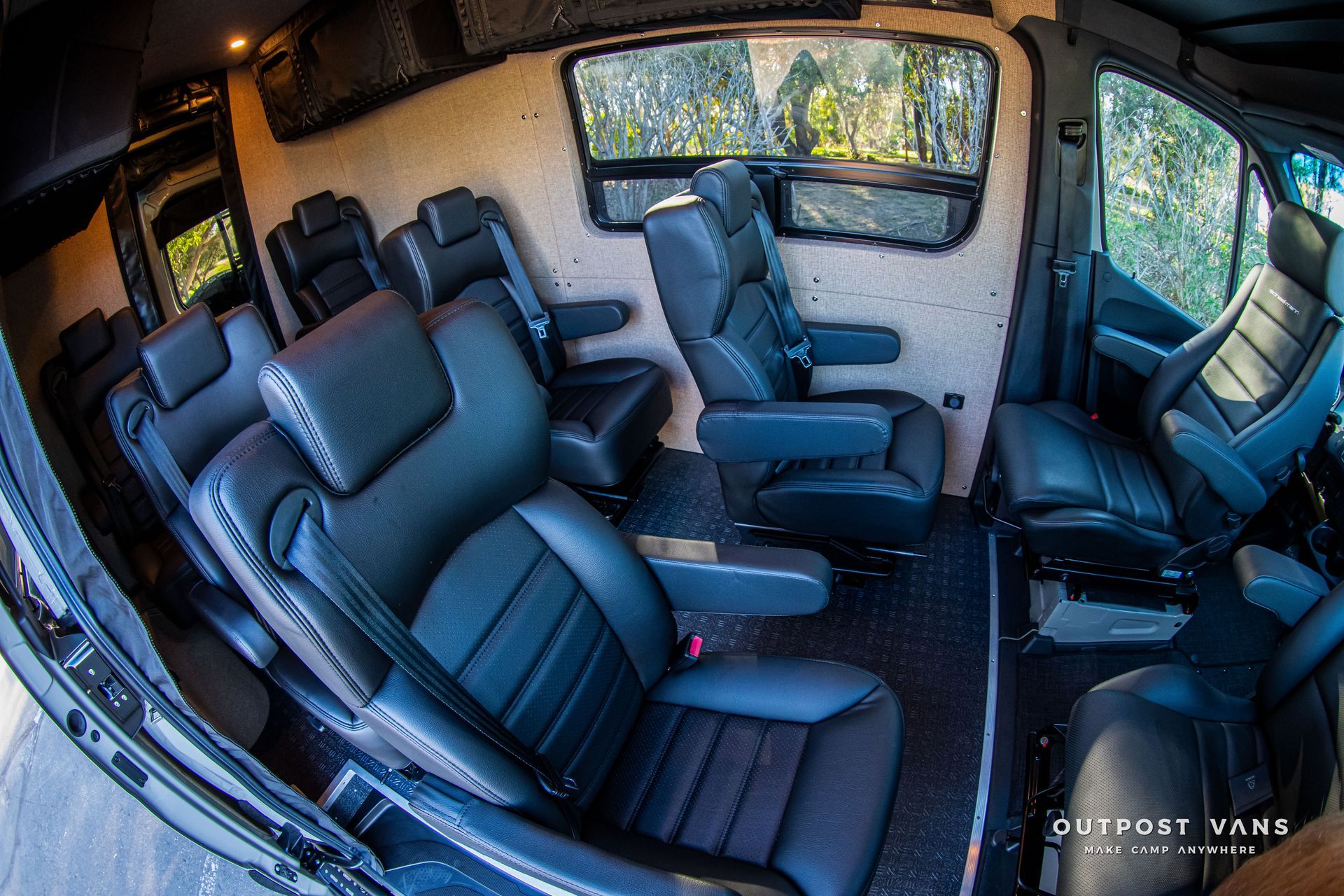 Interior of a luxury van with black leather seats, wood paneling, and large windows.
