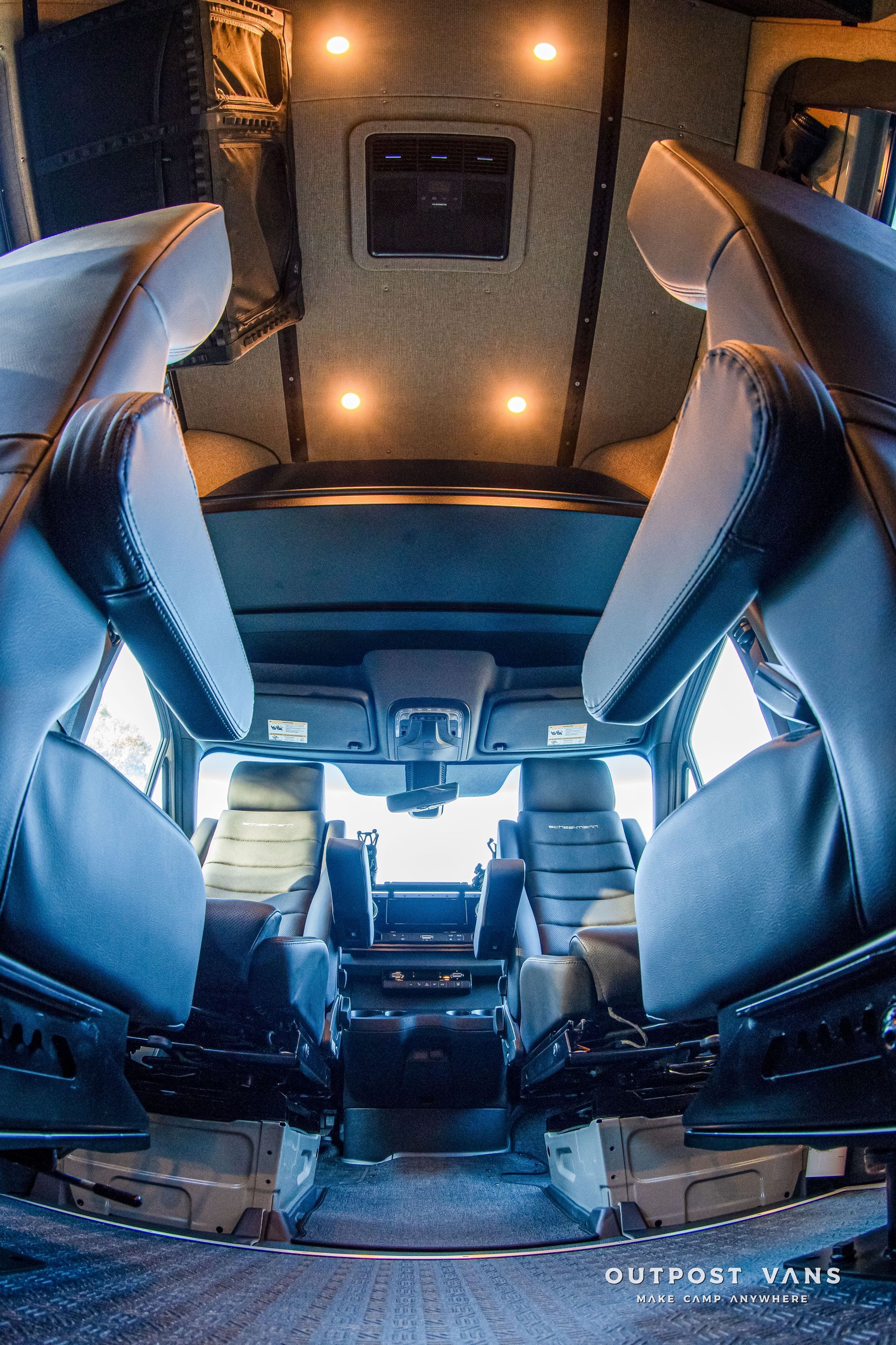 Interior of a customized van. Two rows of gray seats face each other. Overhead lighting illuminates the space.