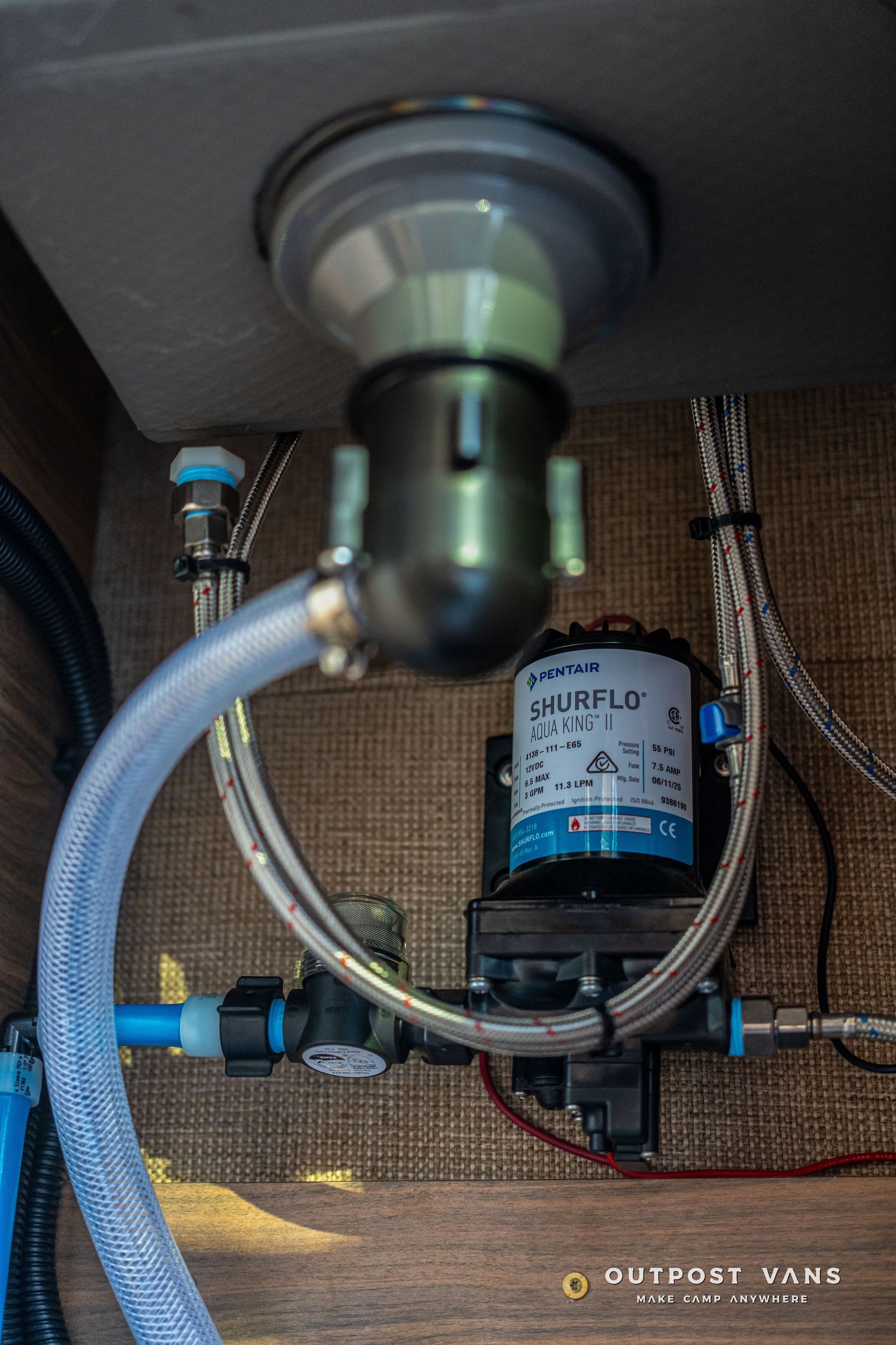 RV plumbing: sink drain, water pump, and various pipes with blue and silver hues.