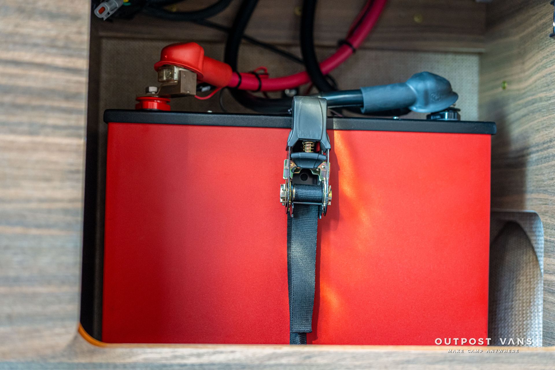 Red battery secured with a strap, with red and black cables connected.