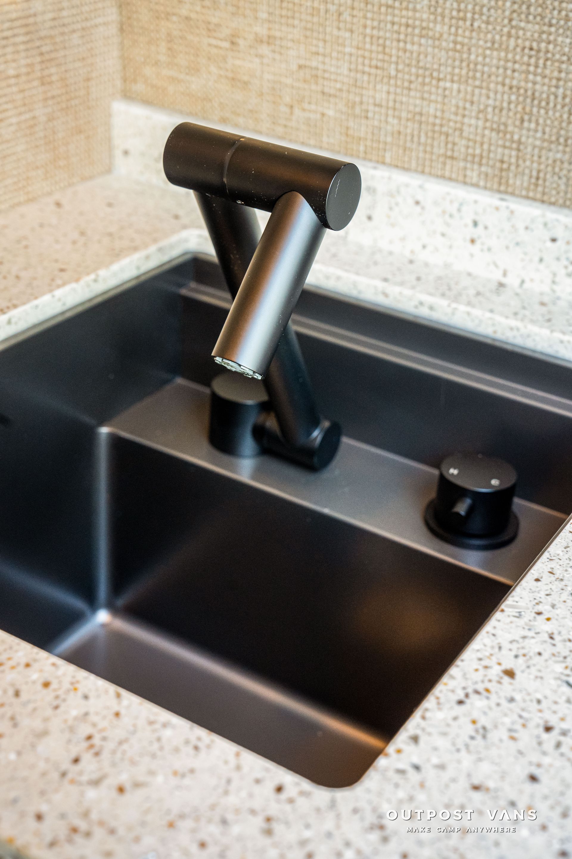 Modern black faucet and sink set in a kitchen, contrasting with a light speckled countertop.