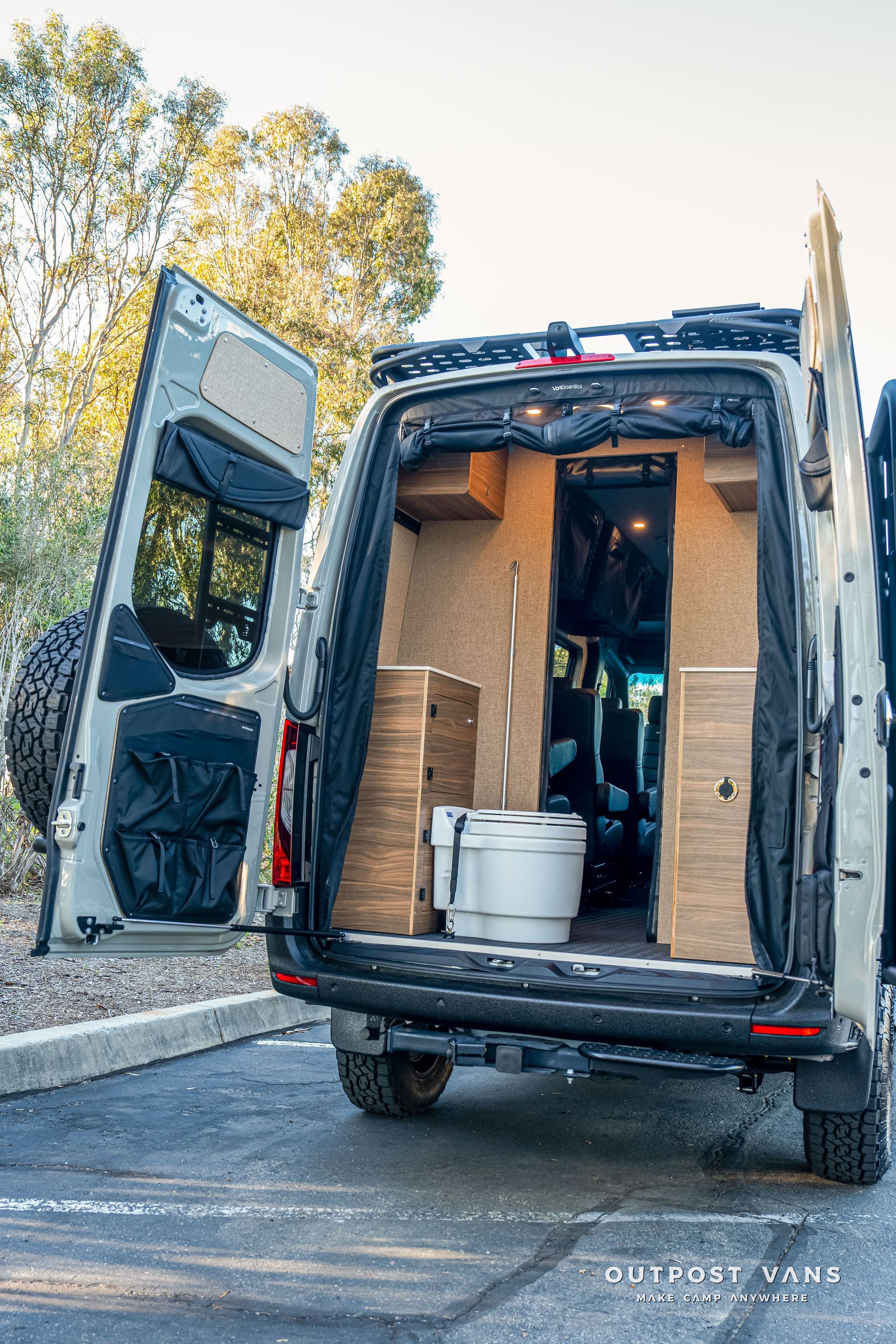 Back of a van with open doors, revealing an interior with a portable toilet and wood paneling.