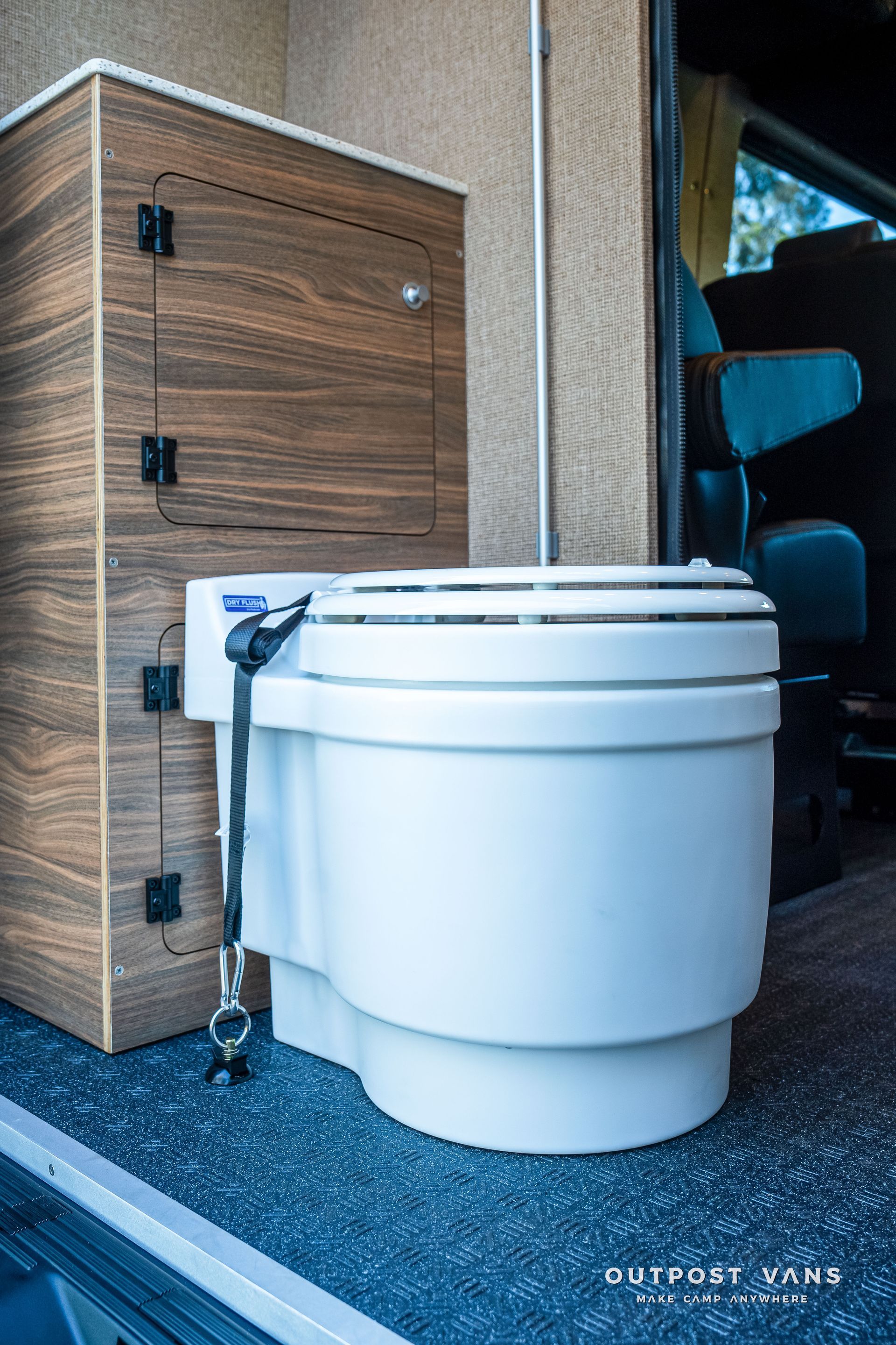 A white composting toilet inside a van next to a wooden cabinet.