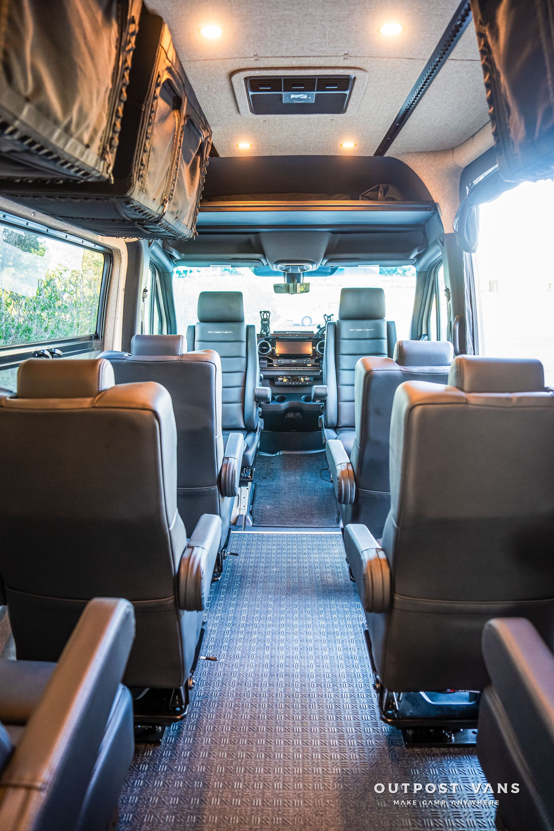 Interior view of a converted van with rows of black seats and a diamond-plate floor.