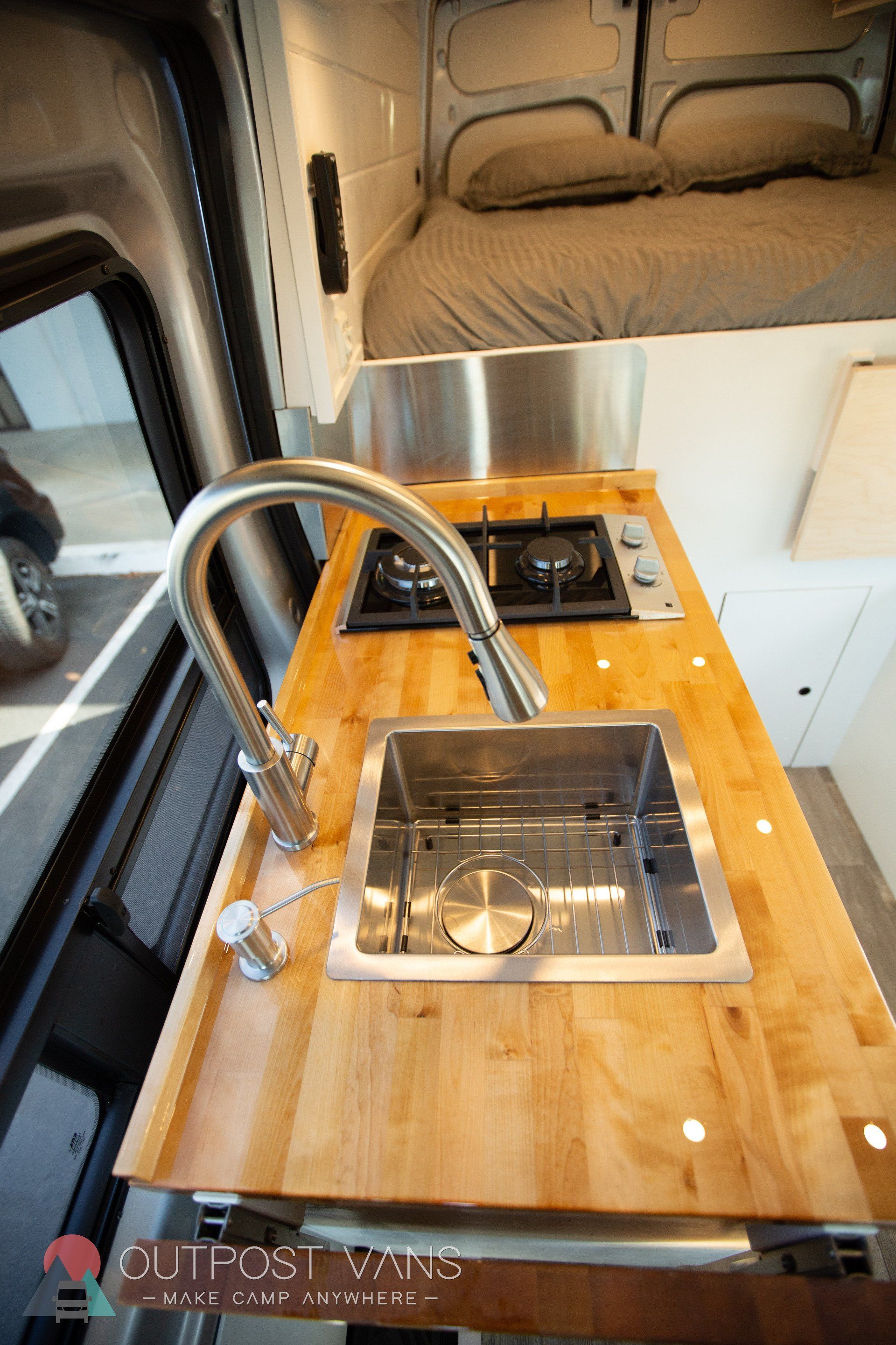 a kitchen in a van with a sink , stove , and bed .