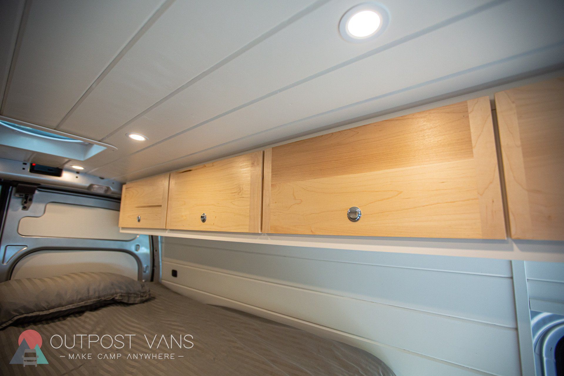 a van with a bed and wooden cabinets on the ceiling .