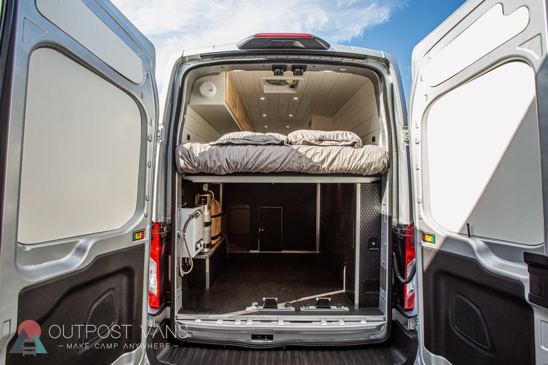 the back of a van with its doors open and a bed in the back .
