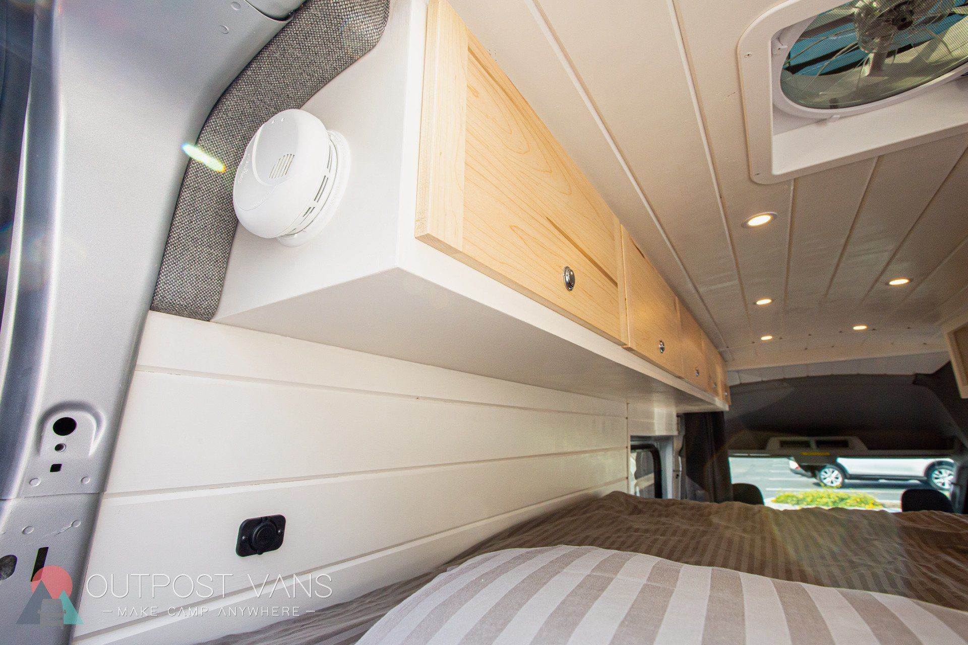 a camper van with a bed , cabinets , and a fan on the ceiling .