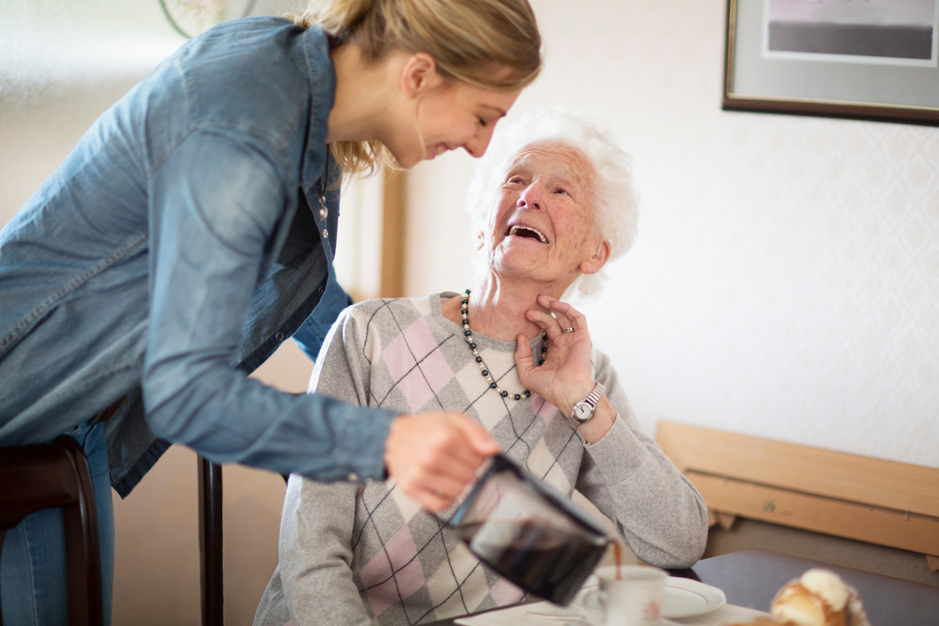 Caregiver helping an elderly woman rise from a chair in a home setting