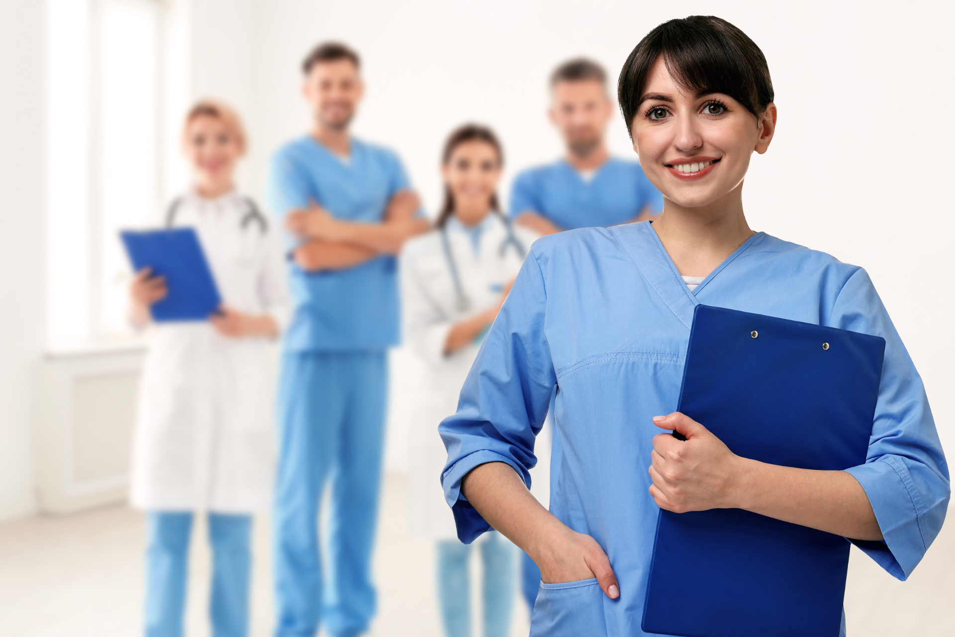 Medical staff in blue scrubs holding clipboards in a bright hospital hallway