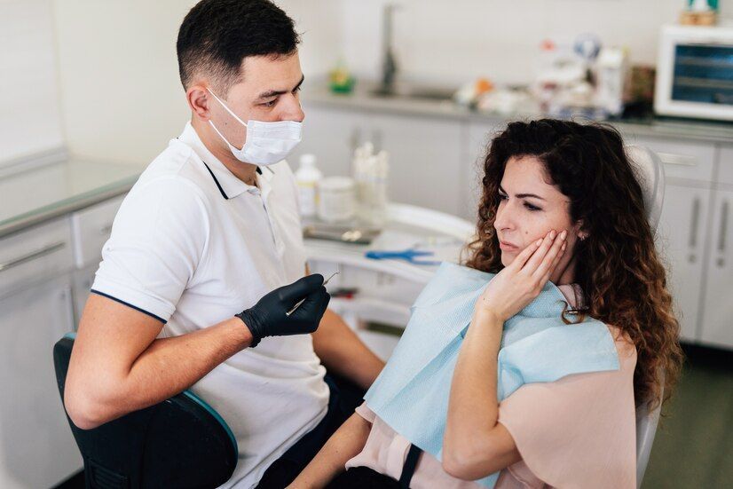 A woman is sitting in a dental chair while a dentist examines her teeth.