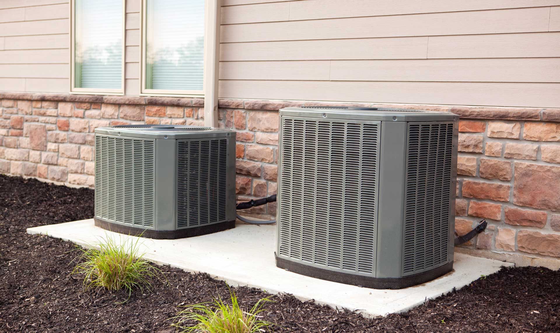 Two air conditioners are sitting on the side of a house.