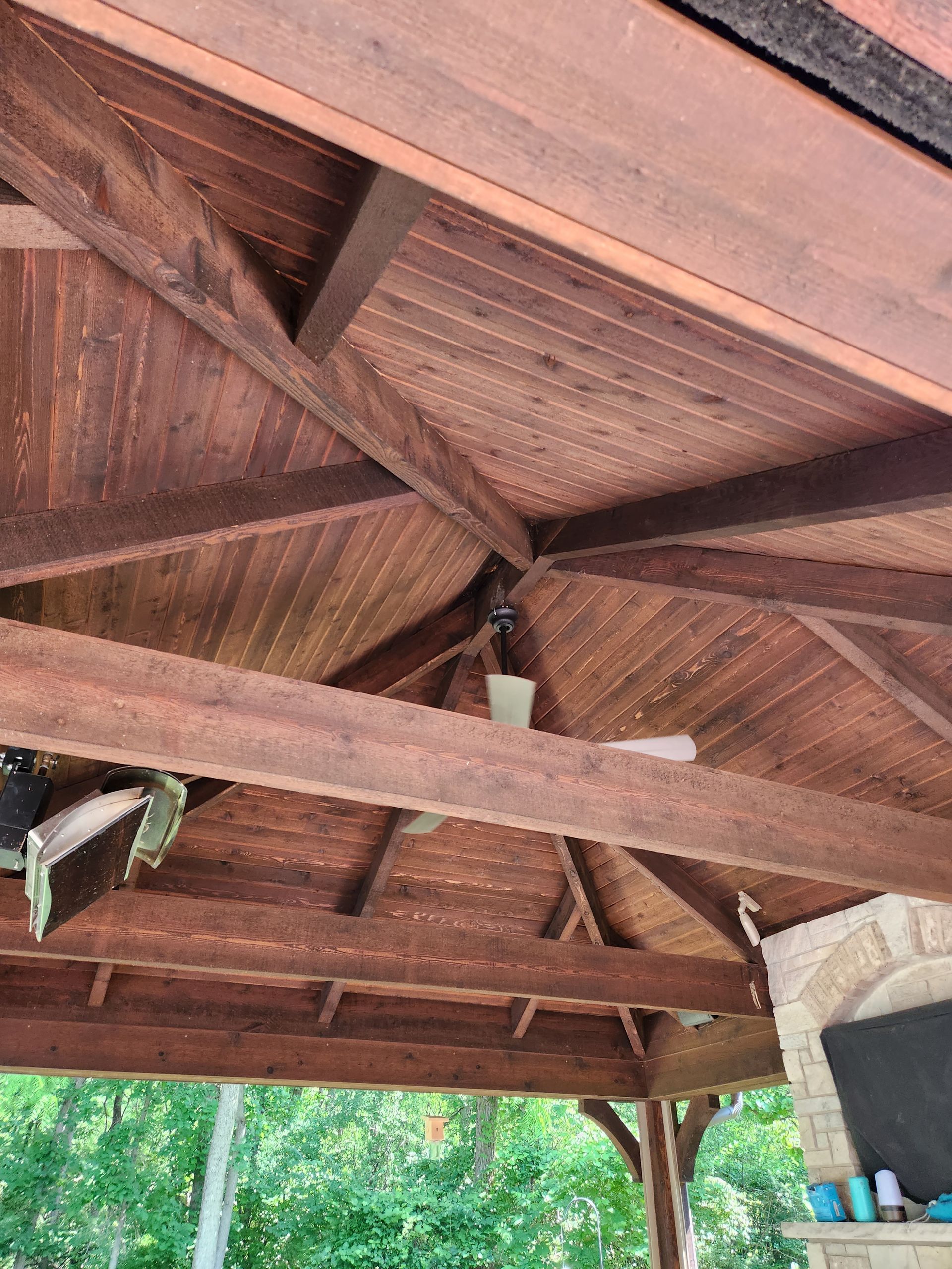 A wooden gazebo with a ceiling fan hanging from it.