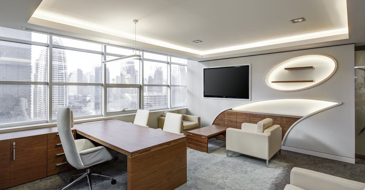 A modern office with a desk , chairs , and a flat screen tv.