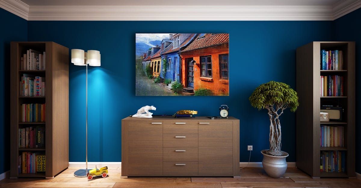 A living room with blue walls , a dresser , bookshelves , a lamp and a painting on the wall.