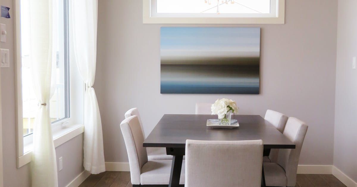 A dining room with a table and chairs and a painting on the wall.