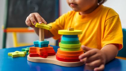 Child stacking colorful wooden rings on a toy sorter in a playroom