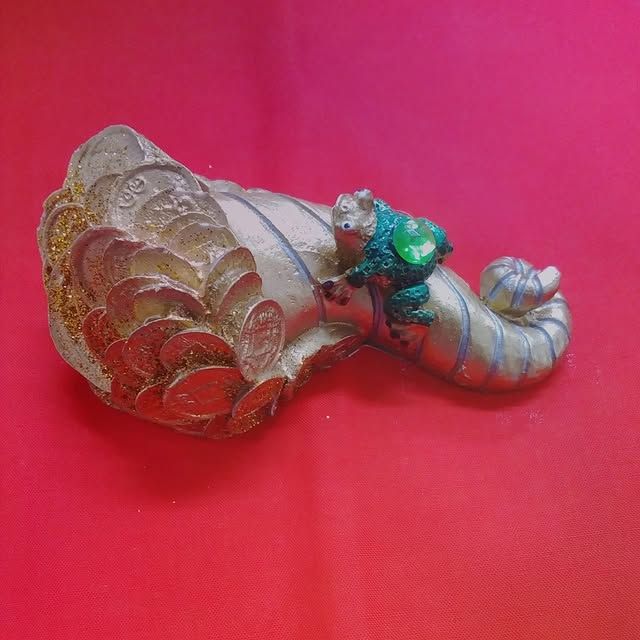 Silver sculpture of a mythical creature with coins and a small frog on a red surface.