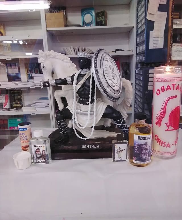 Statue of a warrior on a white horse, surrounded by bottles, a candle, and other ritualistic items.