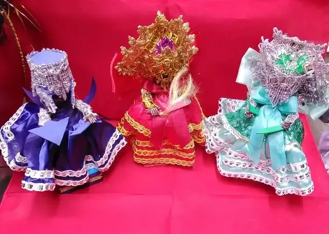Three colorful, decorative dolls with elaborate headdresses and clothing on a pink surface.