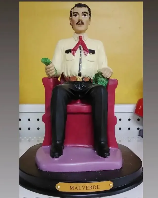 Statue of a man seated in a red chair holding money, labeled