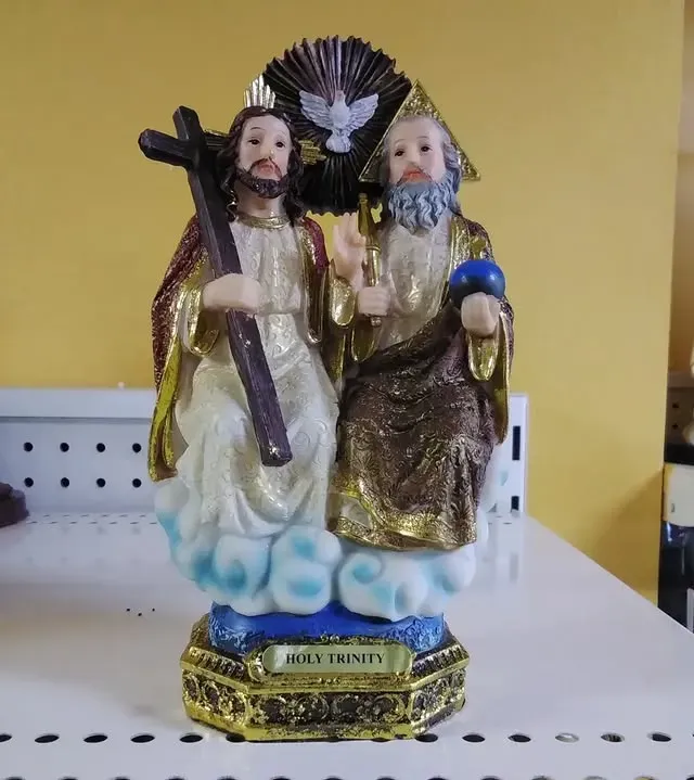 Statue of the Holy Trinity: Jesus with cross, God with globe, and Holy Spirit dove. Gold, white, and blue colors.