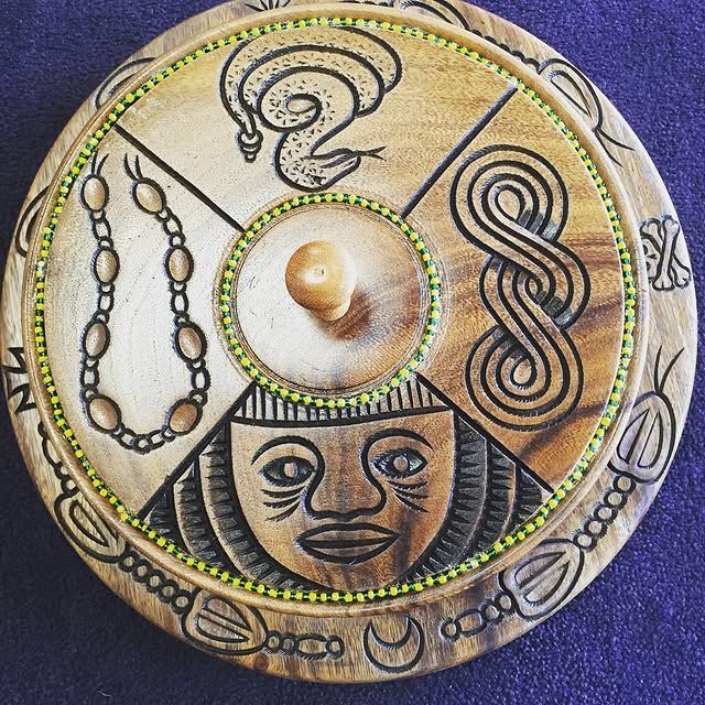 Wooden carved circular container with a face, snake, chain, and intertwined symbol.