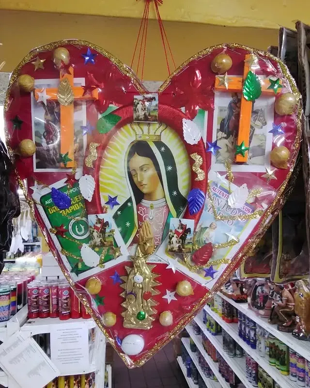 Heart-shaped religious artwork featuring the Virgin of Guadalupe, crosses, and other religious symbols. Red, gold, and white colors.