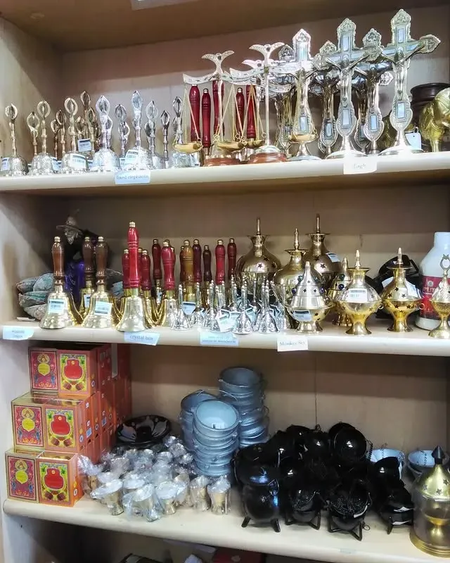 Shelves displaying religious items: crosses, bells, censers, bowls, and boxes in various colors.