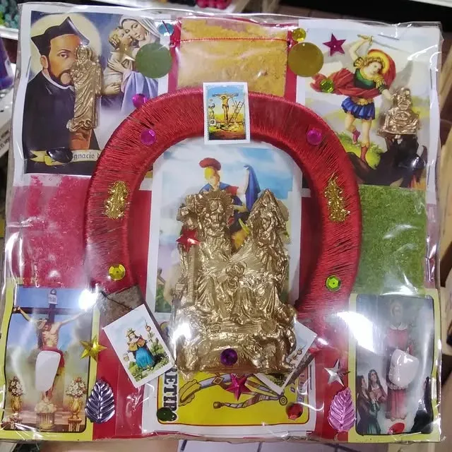 Religious artifact. Multiple figures and images in clear packaging. Red horseshoe-like frame. Various colors and decorations.