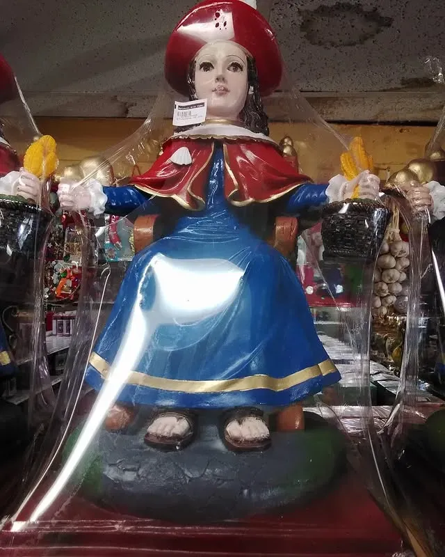 Statue of a woman in blue dress, red cape, and hat, seated on a throne, wrapped in plastic.