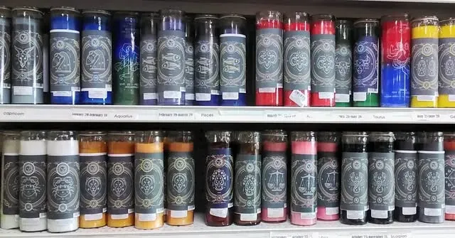 Rows of colorful glass jar candles with labels on a shelf.
