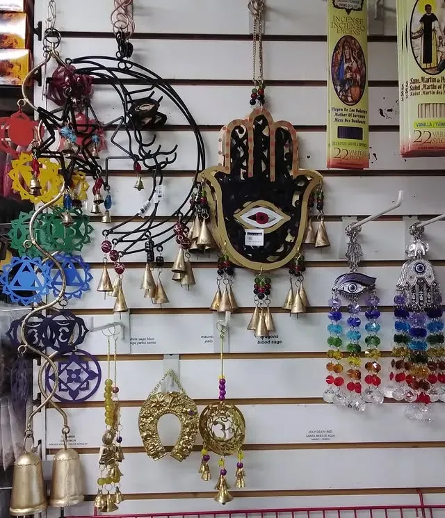 Wall display of spiritual charms, including a Hamsa hand, moon, and chakra symbols, with bells and beads.
