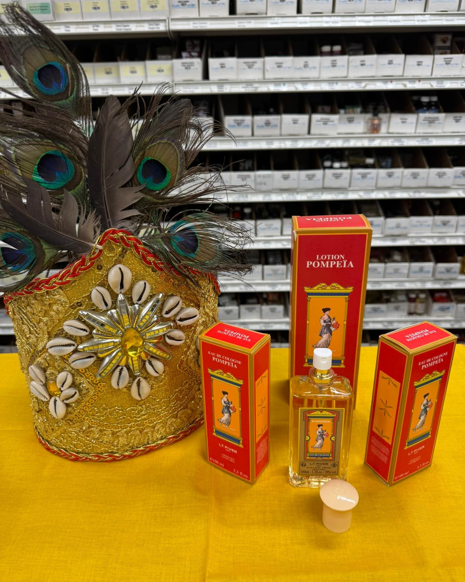 A gold jeweled crown with peacock feathers and three bottles of perfume, all on a yellow cloth.