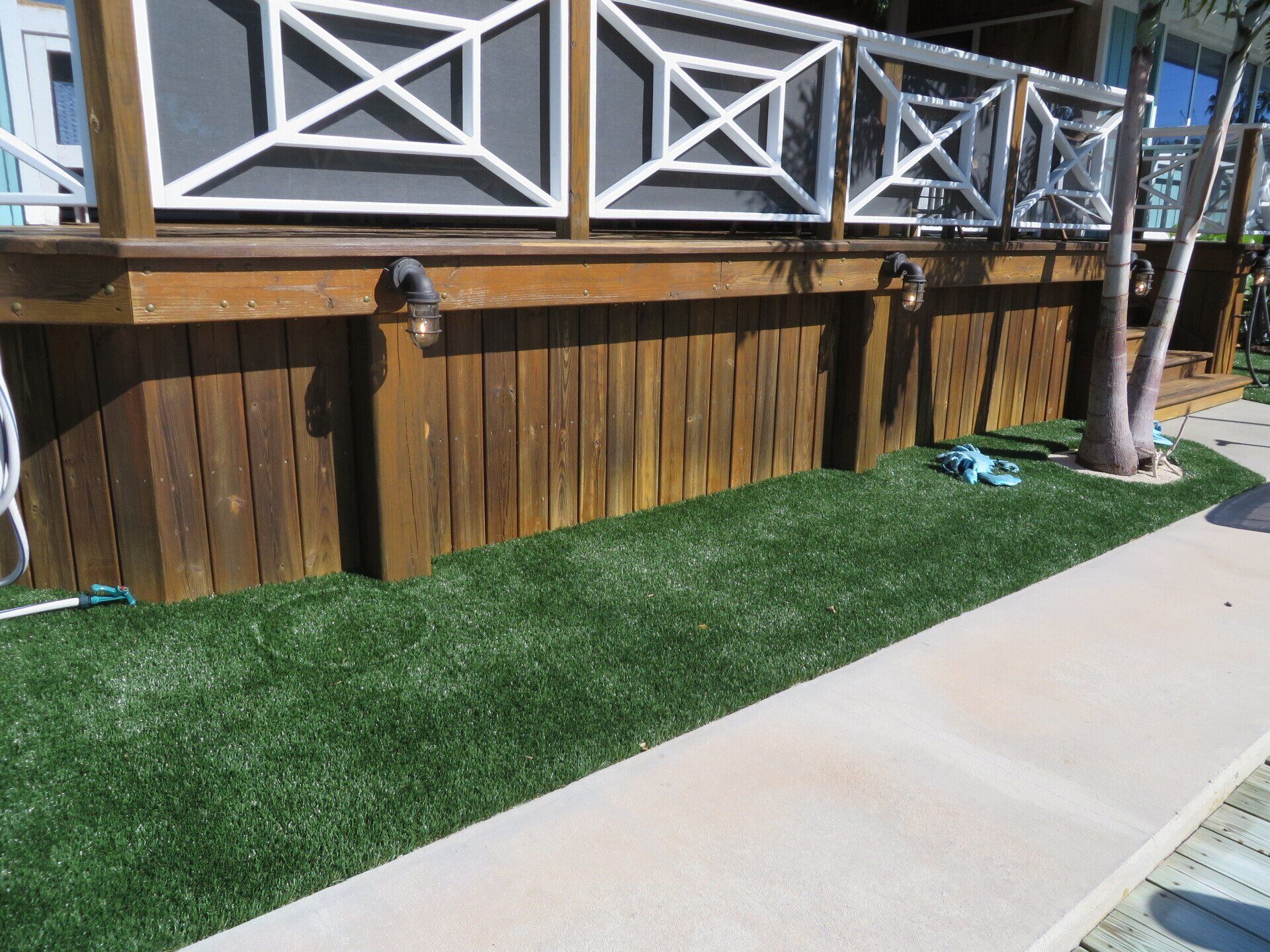 Wooden deck with decorative railing, dark wood siding, and artificial green grass.