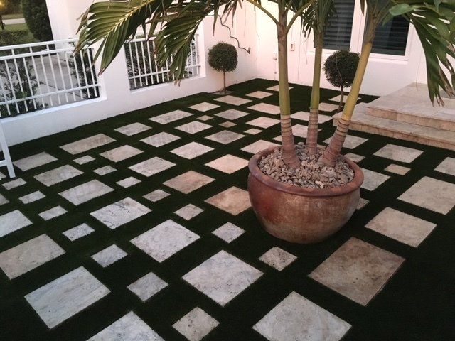 Stone pavers in a grid pattern on artificial turf, with a potted palm tree.
