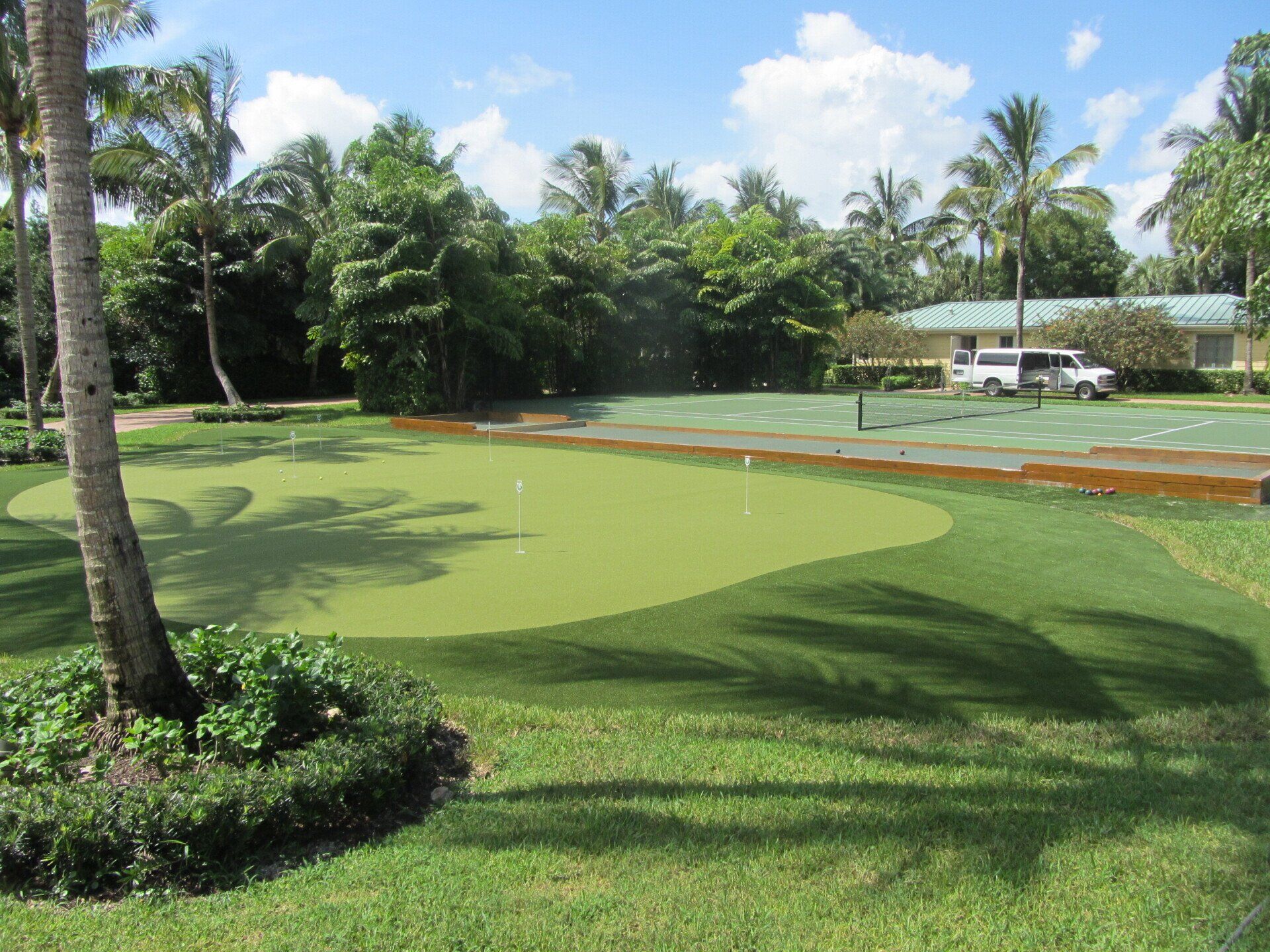 A putting green surrounded by trees and grass, with a white SUV in the background.