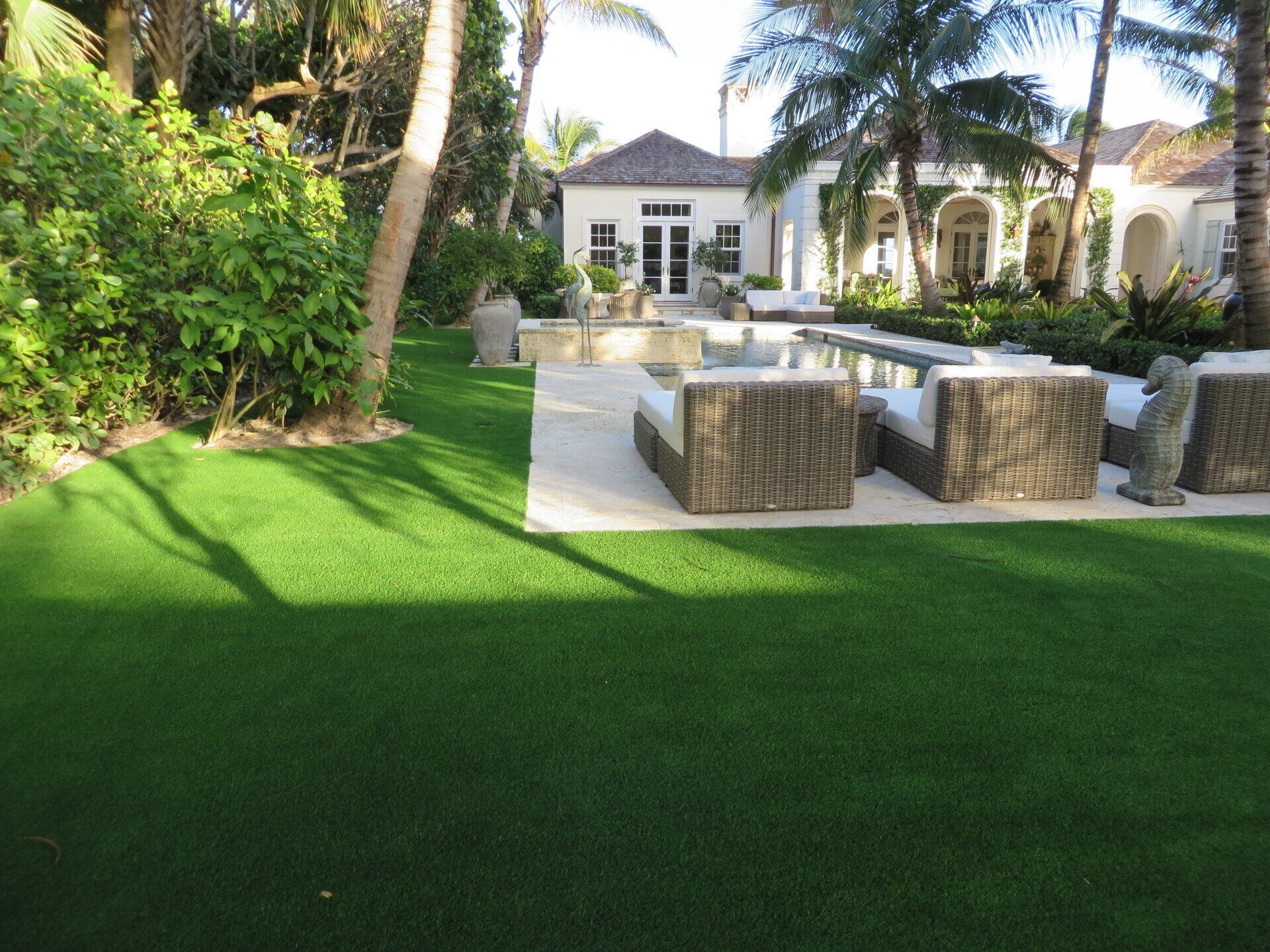 Lush green artificial lawn in front of a luxury house with outdoor seating and a reflecting pool.