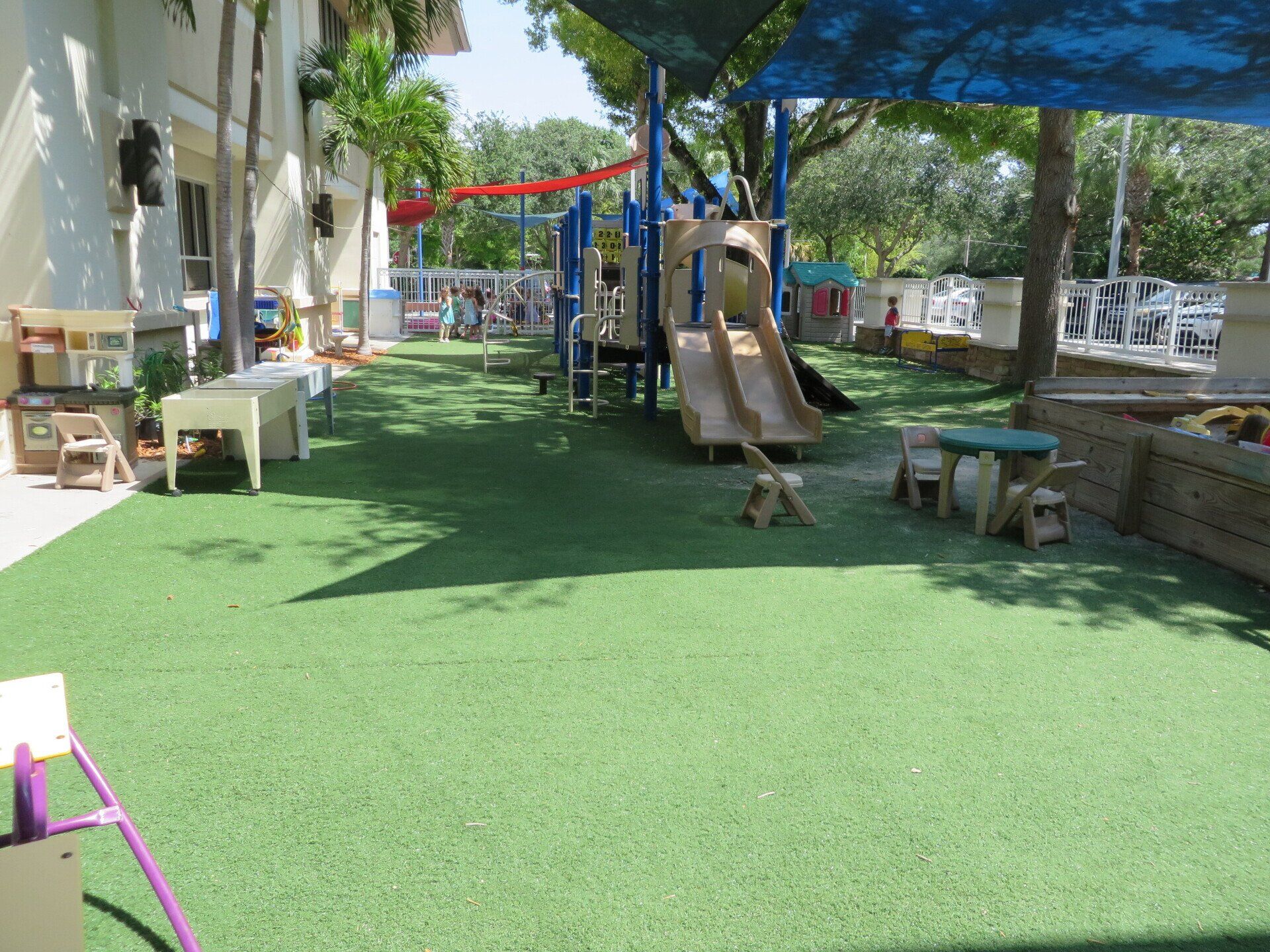 Outdoor playground with a slide, shade canopies, and play equipment on green turf.