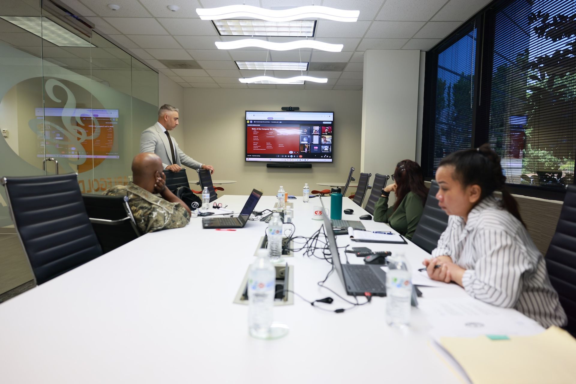 A man in a suit gives a presentation to a team in a modern office, using a whiteboard.