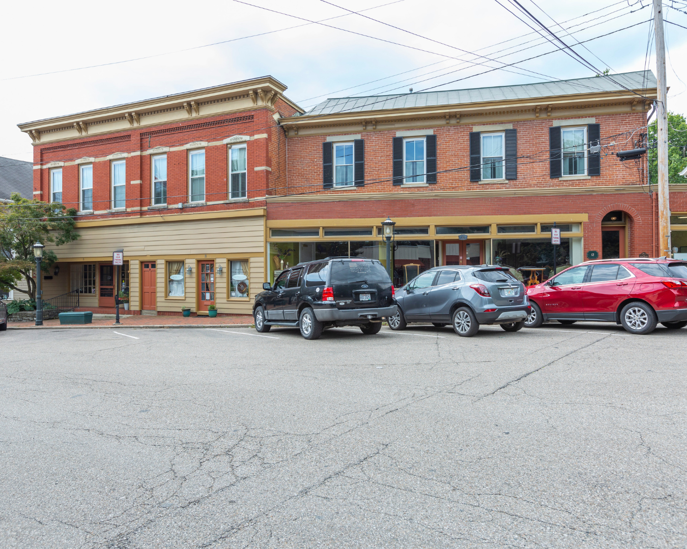 Buildings with brick facades and storefronts, cars parked in front.