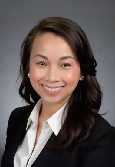 Woman smiling, wearing a white shirt and black blazer against a gray background.