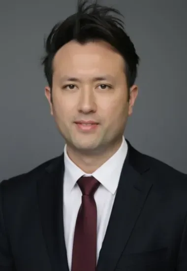Man in a dark suit with a burgundy tie, looking directly at the camera.