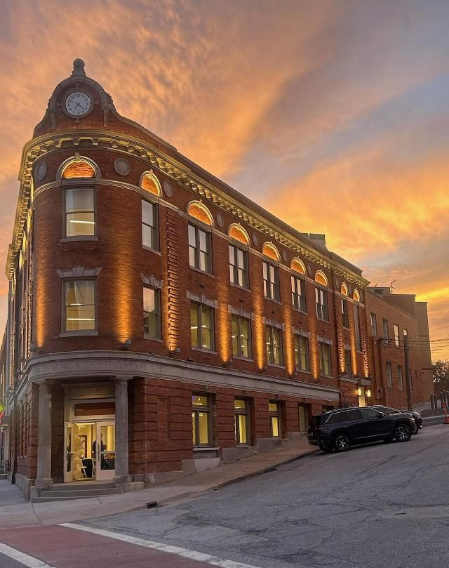 Red brick building with illuminated windows, clock tower at sunset. Black car parked on street. Alton, Il Wedge Building.